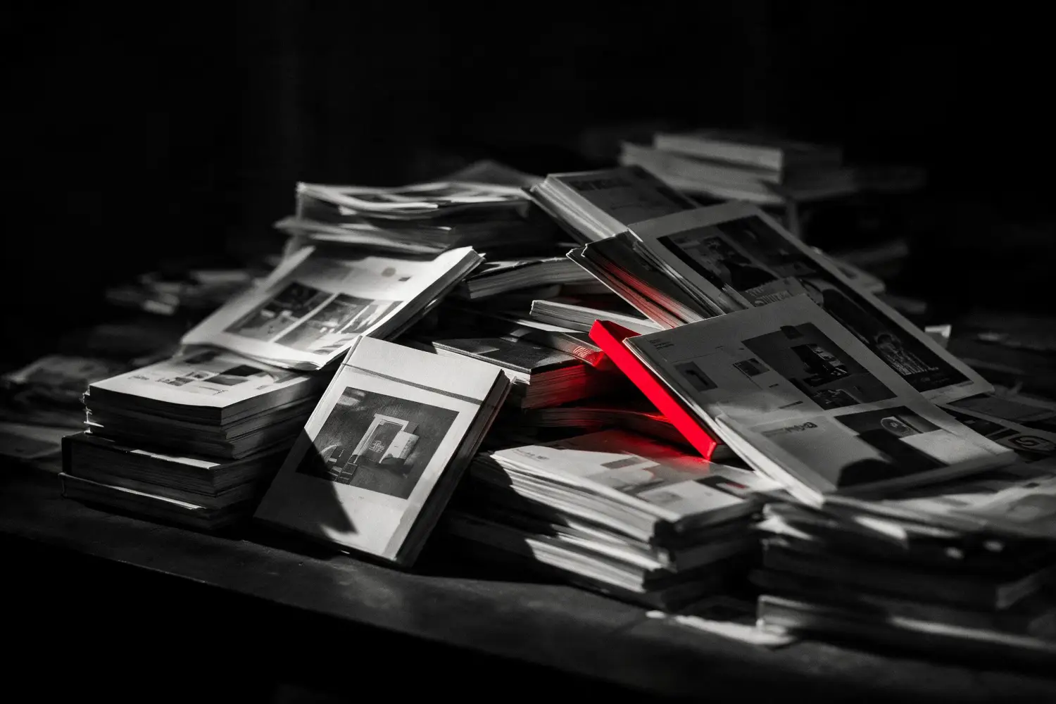 Years of printed project work stacked on a dark table, one volume in red.