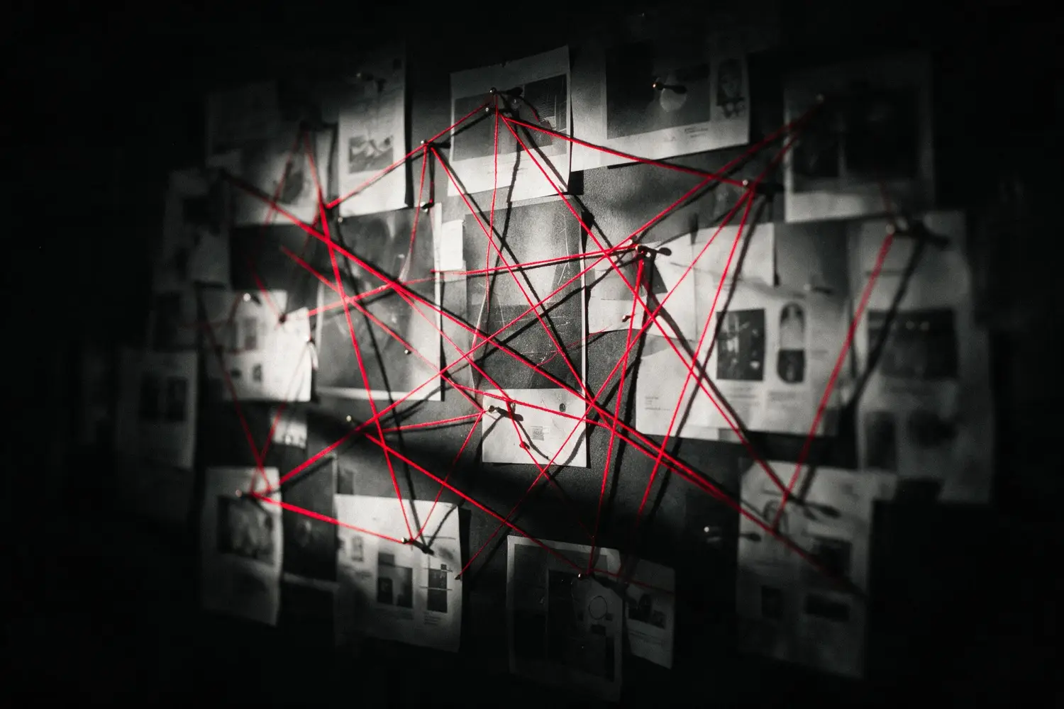 A wall of pinned work with red thread running between the pins in a web that doubles back on itself.
